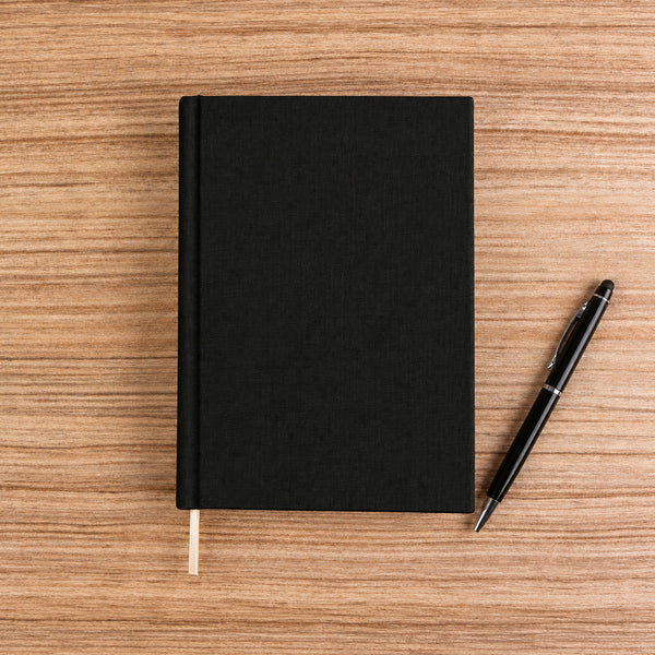 Blank black canvas notebook with pen on a wood desk – plain unprinted cover | Pamusan.com