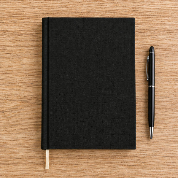 Blank black canvas notebook flat lay on a wood desk with a pen – unprinted A5 cover | Pamusan.com