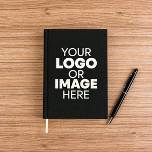 Black canvas notebook with your logo or image printed on the cover, on a wood desk with a pen – A5, 7.9 x 5.5 in (20 x 14 cm) | Pamusan.com