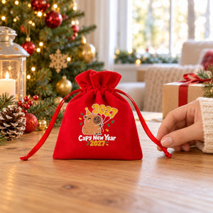 Bolsita de terciopelo rojo con diseño Melchor · Gaspar · Baltasar sobre madera, una mano con manga de punto sujeta la cinta